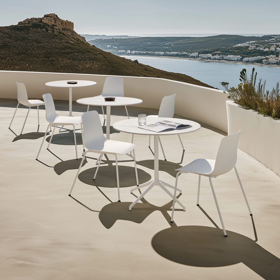 Caféstole Taia Outdoor i hvid ved runde caféborde Barlis Outdoor med udsigt over havet